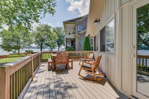 A wooden deck with a table and chairs, overlooking a lake and a building with a balcony. - Pet-Friendly Lake Norman Home with Boat Dock! (Mooresville)
