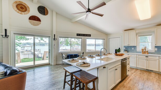 A kitchen with a large island, bar stools, a ceiling fan, and a sign that reads 'EAT, DRINK & BE MERRY'. - Pet-Friendly Lake Norman Home with Boat Dock! (Mooresville)