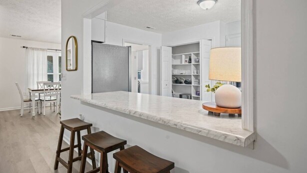Una cocina moderna con encimera de mármol, taburetes de madera y un armario empotrado.