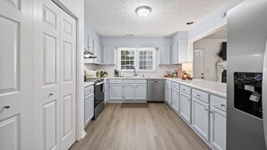 Una cocina con armarios blancos, una ventana, un fregadero, una estufa y un refrigerador.