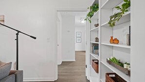 Un pasillo con paredes blancas, una lámpara de pie y una estantería con plantas y objetos decorativos.