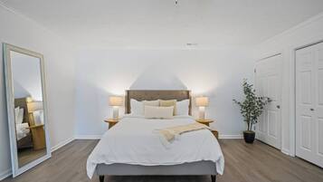 Un dormitorio con una cama, dos mesitas de noche, un espejo, un ventilador de techo y una planta en maceta.