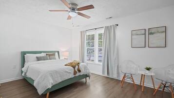 A bedroom with a bed, a ceiling fan, a window with curtains, and a small table with chairs.