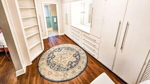 A hallway with a patterned rug, white cabinets, and a door leading to a bathroom.
