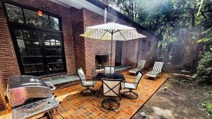 An outdoor patio with a brick floor, a grill, and a table with chairs.