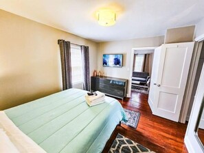 Une chambre à coucher comprenant un lit, une commode, un téléviseur et une porte donnant sur une autre pièce.