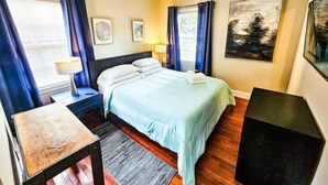 Une chambre à coucher avec un lit, des tables de chevet, un bureau et une fenêtre avec des rideaux.