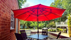 Une terrasse avec un parasol rouge, une table et des chaises.