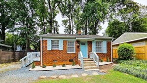 Une maison de plain-pied en briques, dotée d’un porche à l’avant, d’une porte bleue et d’un petit jardin devant, avec un chemin de gravier menant à l’entrée.