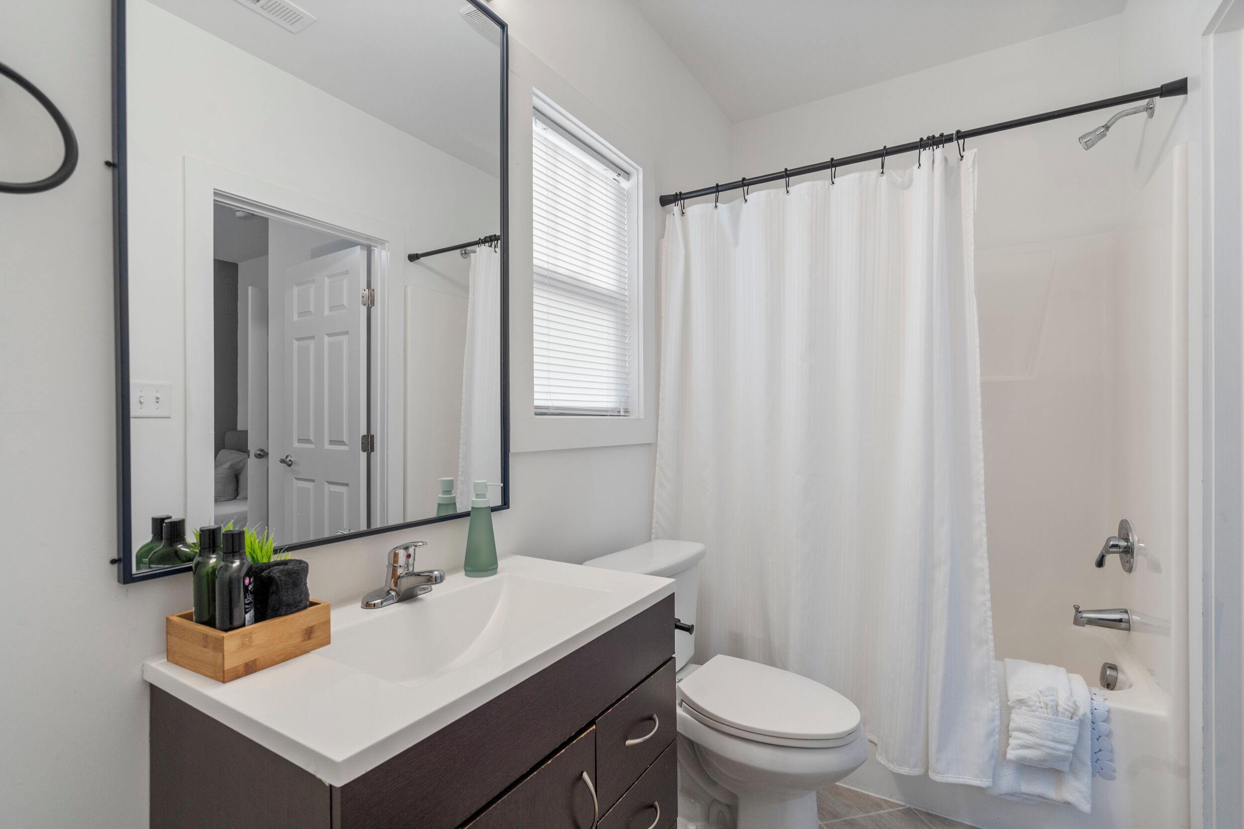 Un bagno moderno con lavandino bianco, mobile bagno scuro, uno specchio grande, un water e una tenda da doccia.