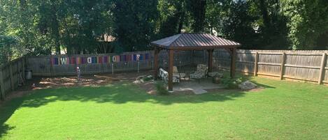 A backyard with a wooden pergola, a fenced play area, and a picnic table.