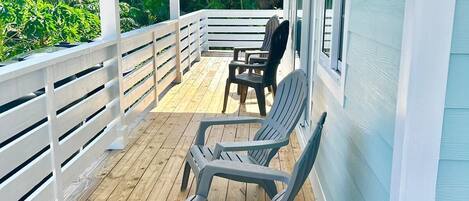 A covered porch with a wooden deck, white railings, and a view of greenery.