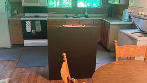 Una cocina con armarios de madera, microondas, estufa y lavaplatos. En primer plano, una mesa de comedor con sillas.