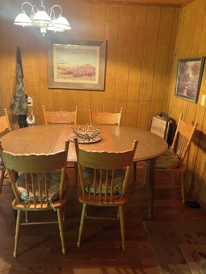 Un comedor con paneles de madera, una mesa redonda, seis sillas y dos lámparas fijadas a la pared.
