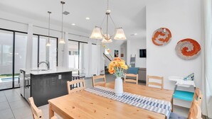 A modern kitchen with a central island, pendant lighting, and a dining area with a wooden table and chairs. - Newly Built Townhouse Close To Disney (Davenport)
