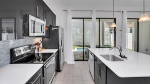 A modern kitchen with a large island, stainless steel appliances, and a view to a glass door leading outside. - Newly Built Townhouse Close To Disney (Davenport)