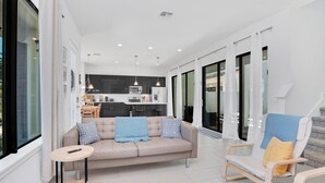 A modern living room with a sofa, a small round table, and a chair. A kitchen is visible in the background. - Newly Built Townhouse Close To Disney (Davenport)