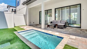 A modern outdoor pool area with a patio, a seating area, and a view of the adjacent building. - Newly Built Townhouse Close To Disney (Davenport)