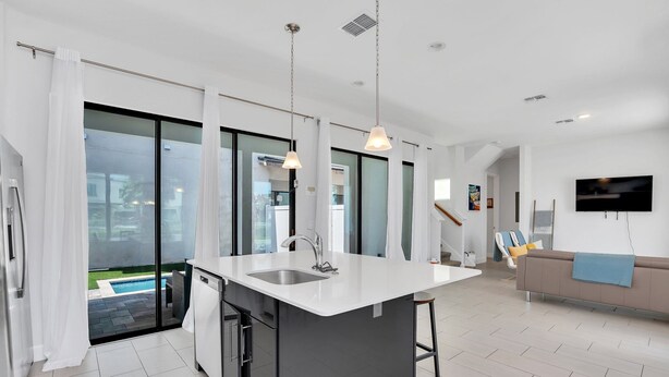 A modern kitchen with a central island, a built-in dishwasher, and a large window overlooking a pool. - Newly Built Townhouse Close To Disney (Davenport)