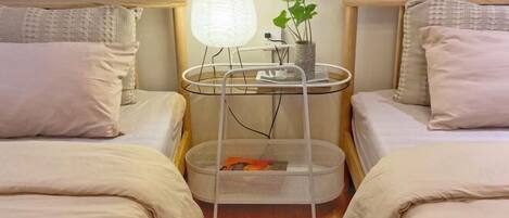 Een hotelkamer met twee bedden, een nachtkastje met lamp, een kleine plant en een mand.