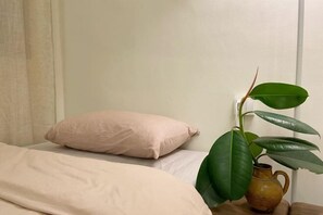 A bed with a beige blanket and a single pink pillow. A green plant with broad leaves is placed on a wooden table beside the bed. - Yangshuo Yijian Huashu Inn (West Street) (Yangshuo)