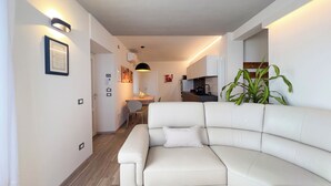 A modern living room with a white sofa, a dining area with a table and chairs, and a kitchen in the background. - Casa Camelia: your luxury apartment in the heart of Cinque Terre (Volastra)