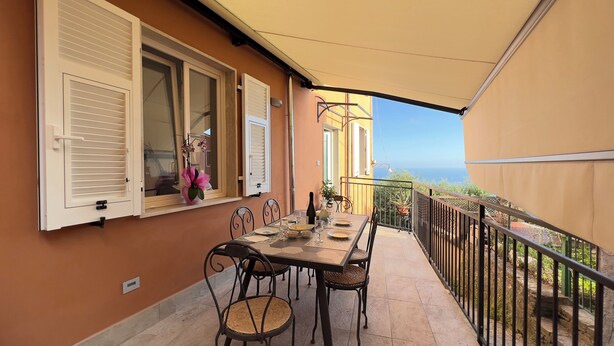 A balcony with a table set for dining, chairs, and a potted plant. - Casa Camelia: your luxury apartment in the heart of Cinque Terre (Volastra)