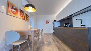 A modern kitchen with a built-in oven, a coffee machine, and a sink. There is a dining area with a wooden table and two chairs. - Casa Camelia: your luxury apartment in the heart of Cinque Terre (Volastra)