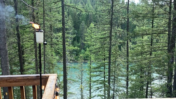 A wooden deck with a view of a forest and a river. - Secluded riverfront RV 7 Miles from Glacier National Park! (Coram)