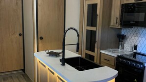 A modern kitchen with a central island, a stove, a microwave, and wooden cabinetry. - Secluded riverfront RV 7 Miles from Glacier National Park! (Coram)