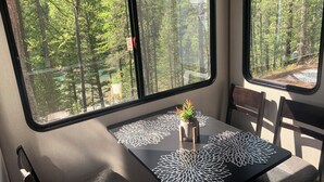 A table with a potted plant and decorative tableware, set against a forest view from a cabin. - Secluded riverfront RV 7 Miles from Glacier National Park! (Coram)