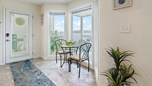 Ein sonnendurchflutetes Zimmer mit Esstisch und Stühlen, einer Topfpflanze und Blick durch große Fenster.
