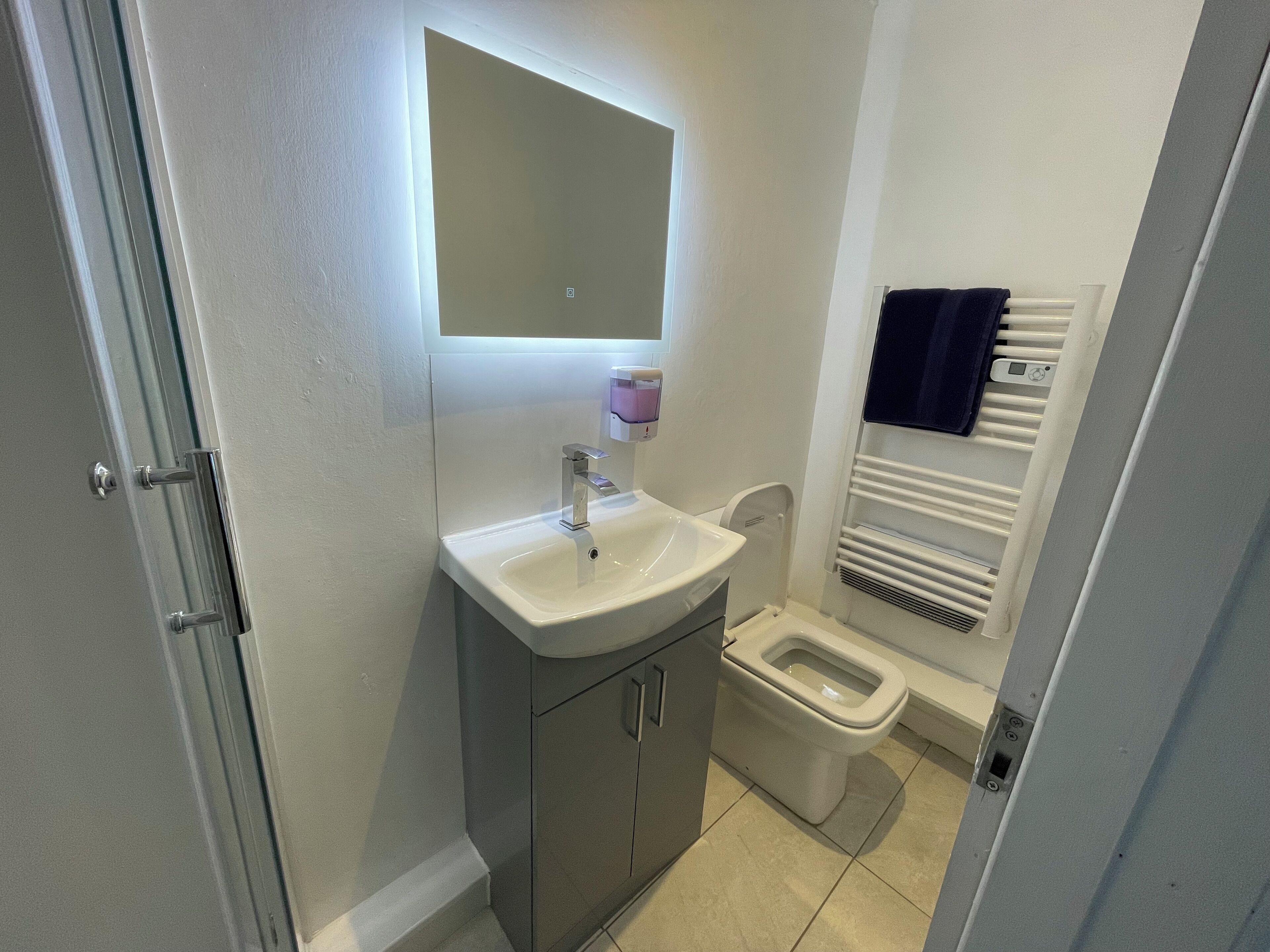 Une petite salle de bain avec un lavabo blanc, un miroir au-dessus, des toilettes et un porte-serviettes.