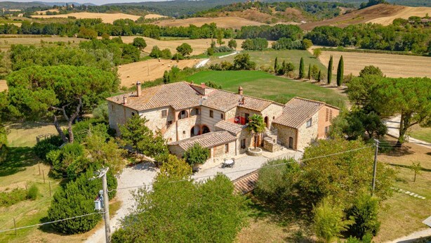 Un bâtiment en pierre, surmonté d’un toit en tuiles, entouré d’arbres et de champs.