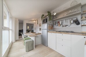 A modern kitchen with white cabinets, a stainless steel refrigerator, a gas stove, and hanging pots.