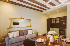 Zona pranzo con tavolo rotondo, sedie, divano, uno specchio e una cucina sullo sfondo.