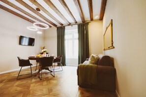 A room with a wooden ceiling, a dining table with chairs, a sofa, a TV mounted on the wall, and a window with curtains.