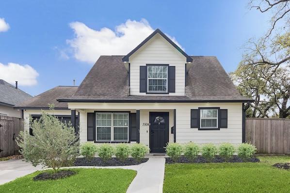 A two-story house with a front entrance, a small front yard, and a wooden fence.
