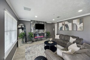 A modern living room with a fireplace, a large flat-screen TV, and a sectional sofa.