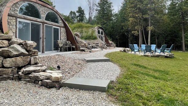 Una cabaña rústica con fachada de piedra, un gran ventanal arqueado y una escalera de piedra que lleva a una terraza.