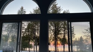 Una habitación con amplios ventanales arqueados que dan a un bosque y a una puesta de sol.