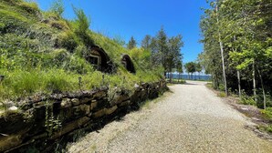 Un camino de grava que conduce a casas de piedra tradicionales con tejados de paja, rodeado de abundante vegetación y árboles.