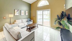 Un salon avec un canapé, une table basse et une lampe. Une grande fenêtre offre une vue sur une piscine.