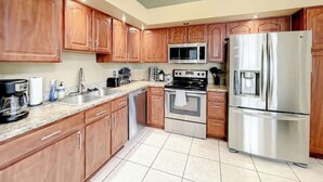Une cuisine moderne avec des meubles en bois, des appareils électroménagers en acier inoxydable et un sol carrelé.