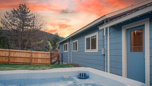 Een achtertuin met een jacuzzi, houten omheining en een huis met een blauwe gevel.