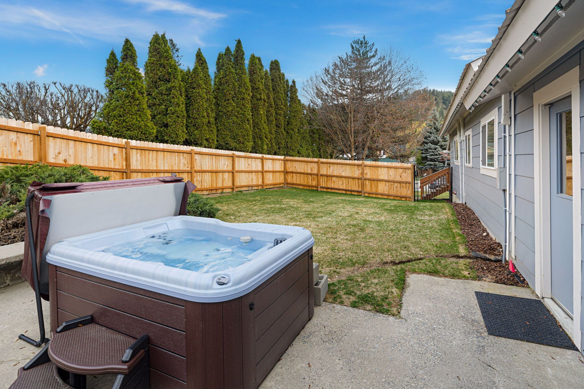 A backyard with a hot tub, wooden fence, and a house.