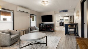 Een moderne woonkamer met een flatscreen televisie, een bank, een salontafel en een keuken in de achtergrond.