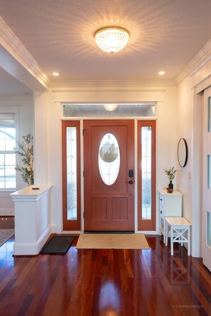 Una entrada bien iluminada con una puerta de madera, un banco blanco y una pequeña mesa con una planta.