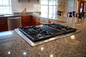 Una cocina con encimeras de granito, estufa de acero inoxidable, armarios de madera y lavavajillas.