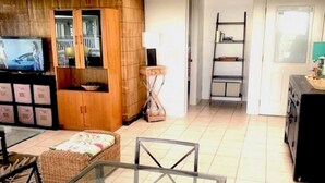 A modern living room with a glass dining table, a sofa, and a kitchen area with a TV and wooden cabinets. -  Walk to White Sands Beach   Ocean view 2 Bedroom with pool (Kailua-Kona)